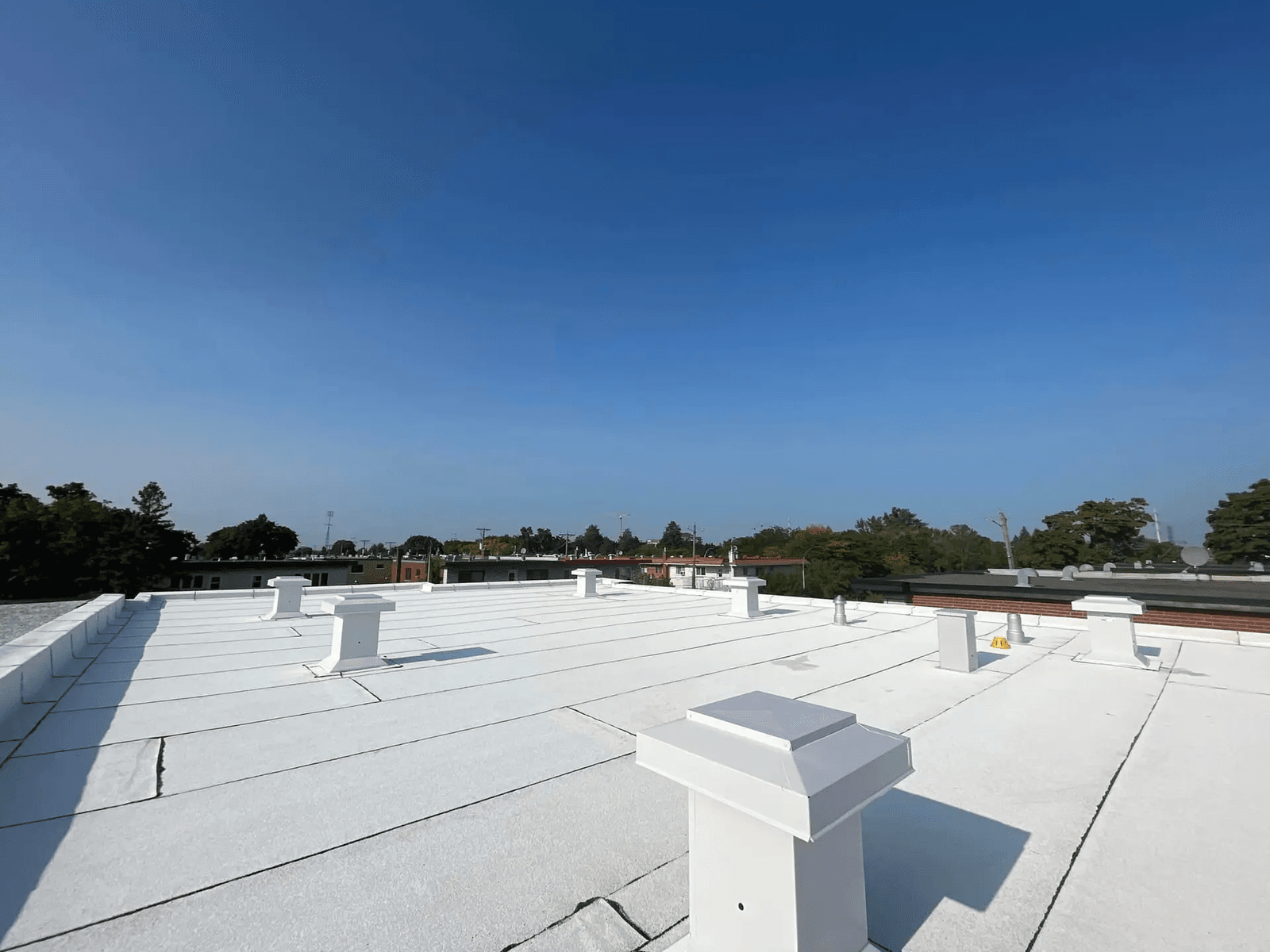 Toiture plate recouverte d'une membrane blanche avec plusieurs évents de ventilation sous un ciel dégagé.