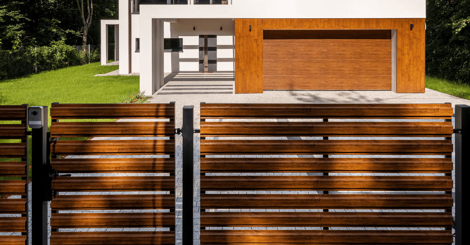 Clôture moderne en bois à lattes horizontales avec poteaux métalliques noirs devant une maison contemporaine dotée d’une porte de garage en bois et d’une entrée pavée.