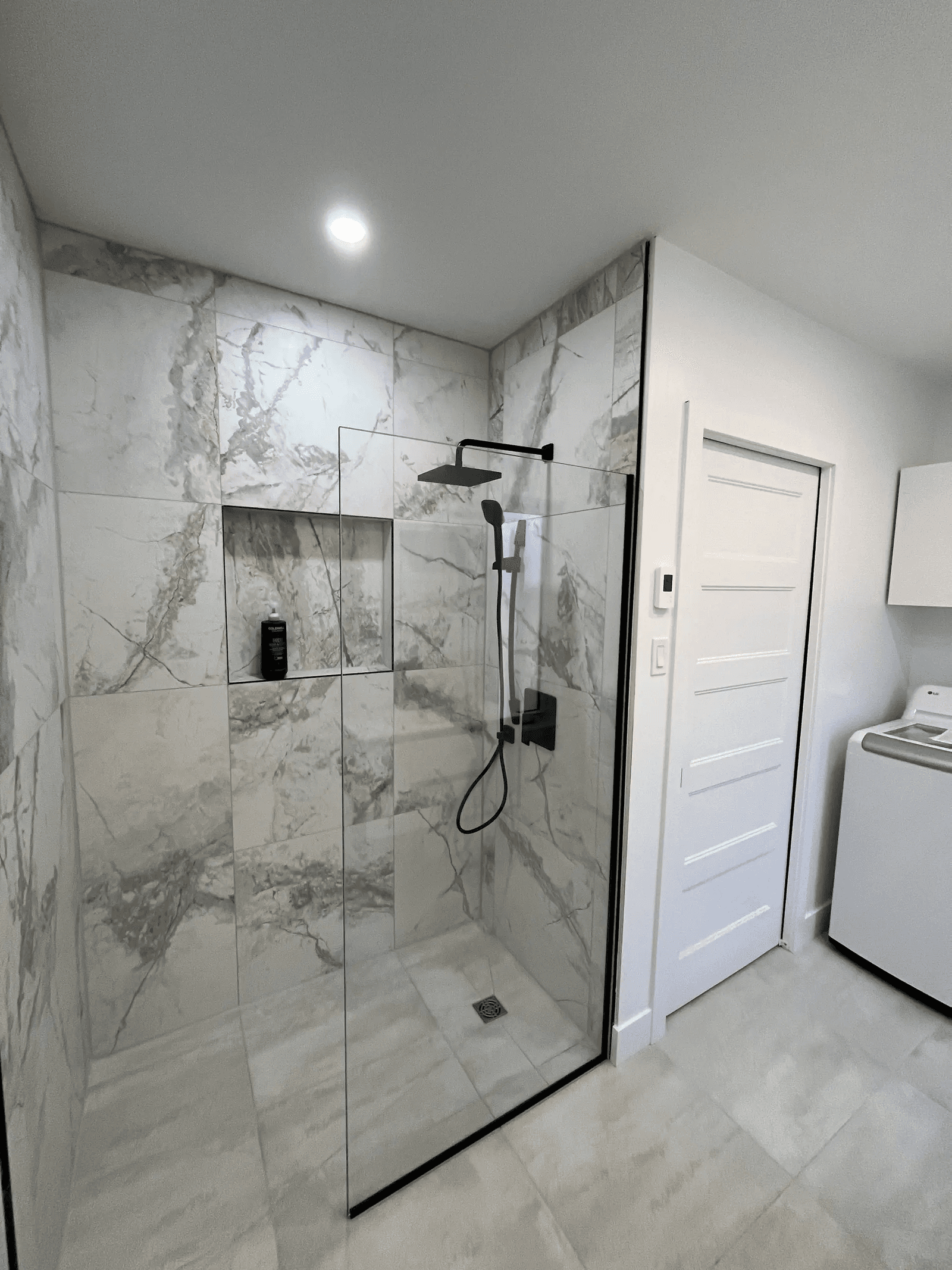 Douche moderne à l’italienne avec parois vitrées, carrelage effet marbre blanc, niche murale et robinetterie noire dans une salle de bain rénovée