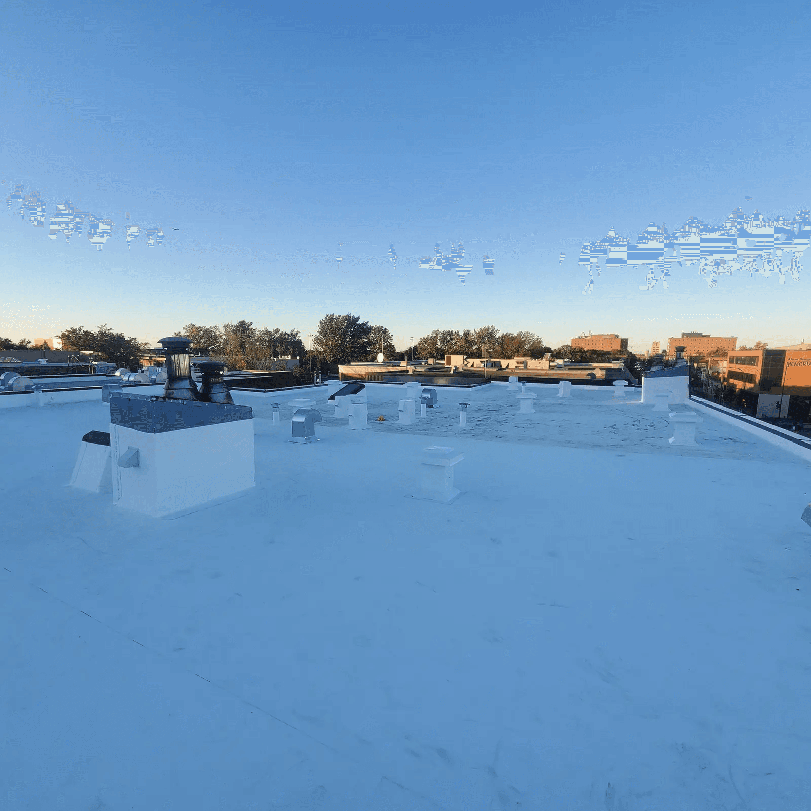 Grand toit plat recouvert d’une membrane blanche réfléchissante avec plusieurs évents, sorties de ventilation et équipements de toiture en milieu urbain