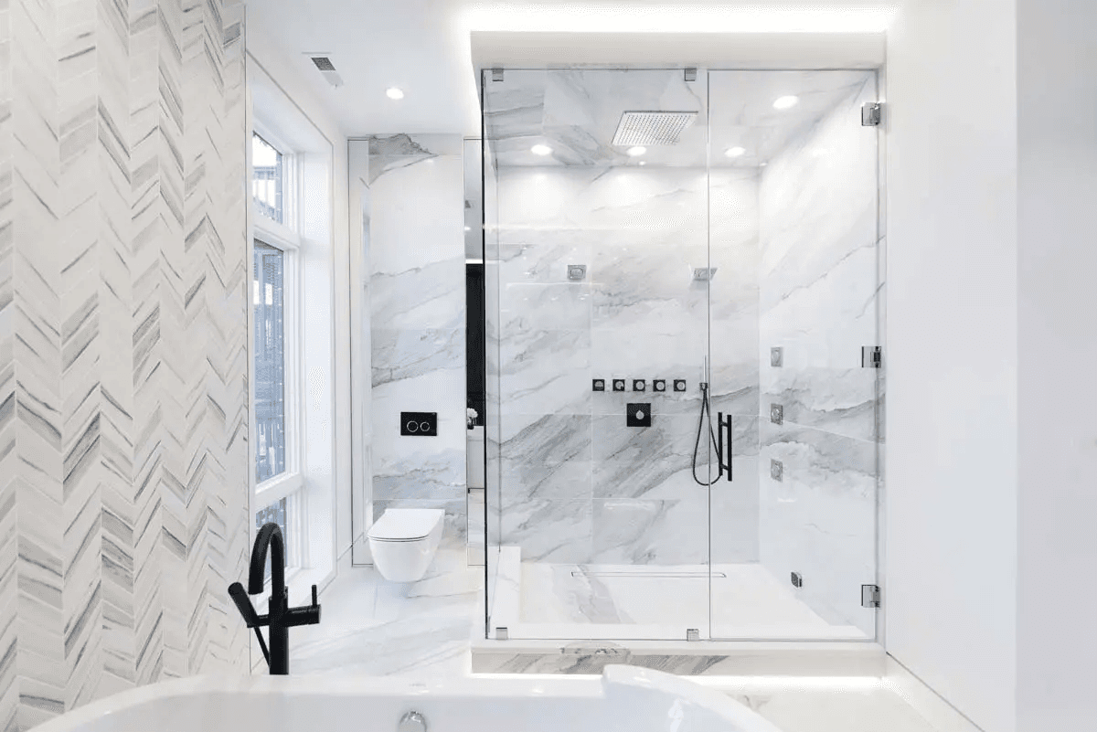Salle de bain moderne et luxueuse avec douche vitrée, murs en marbre blanc, carrelage chevron, robinetterie noire, baignoire blanche et éclairage encastré pour un design épuré et lumineux