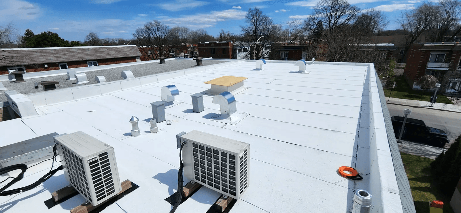 Toit plat blanc d’un immeuble résidentiel avec unités de climatisation, évents métalliques et ouvertures de ventilation