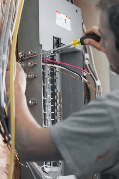 Électricien effectuant le raccordement et l’installation de câbles dans un panneau électrique résidentiel ouvert à l’aide d’un tournevis