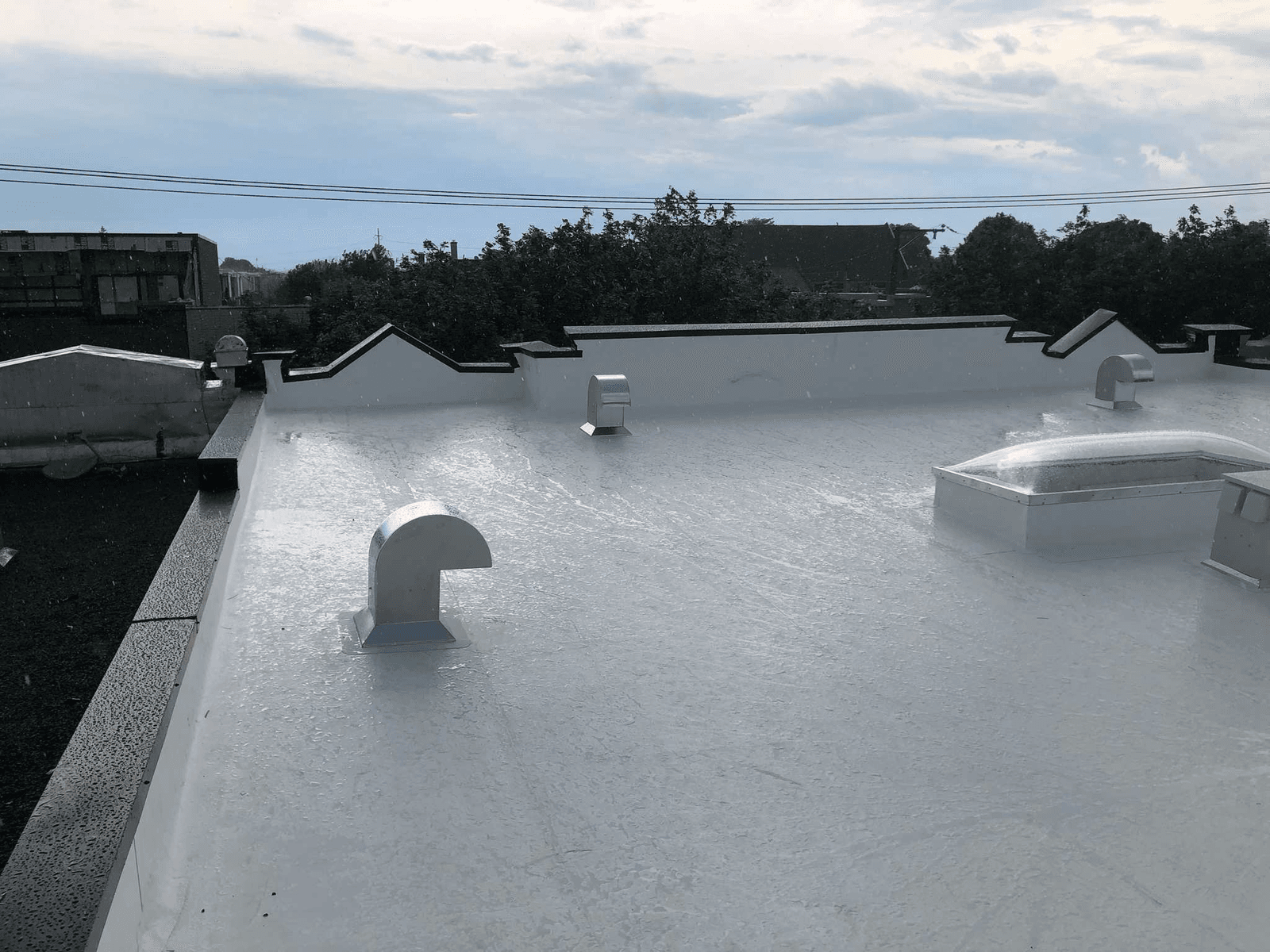 Toiture plate blanche avec revêtement imperméabilisant, ouvertures de ventilation et puits de lumière sous la pluie.