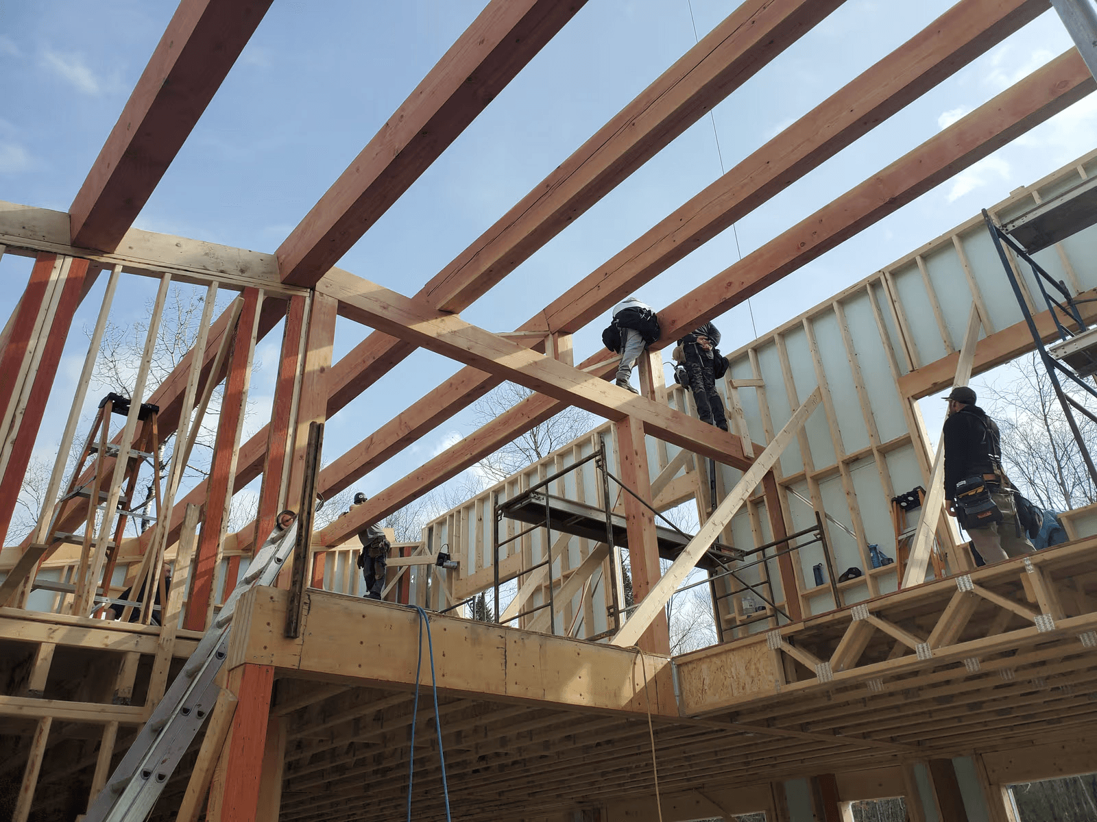 Travaux de charpente intérieure avec poutres en bois massif, murs à ossature et ouvriers installant la structure d’une maison en construction.