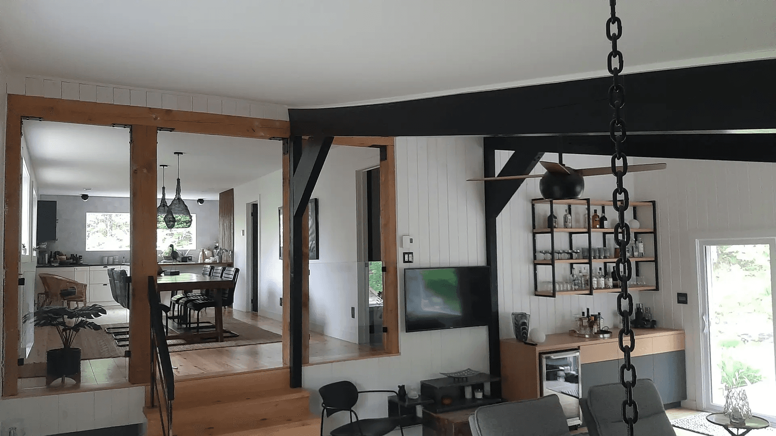 Intérieur de maison rénovée avec poutres de bois apparentes, structure noire, salon ouvert, salle à manger et cuisine moderne dans un espace à aire ouverte&nbsp;