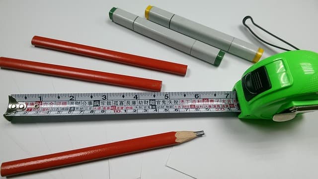 Ruban à mesurer vert déployé avec des crayons de menuisier rouges et des marqueurs sur un plan de travail blanc