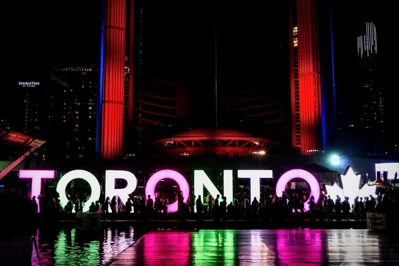 Le célèbre signe TORONTO illuminé en rose et vert la nuit devant l'hôtel de ville avec une foule de personnes