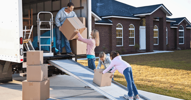 Une famille décharge des cartons d’un camion de déménagement devant une maison en briques.