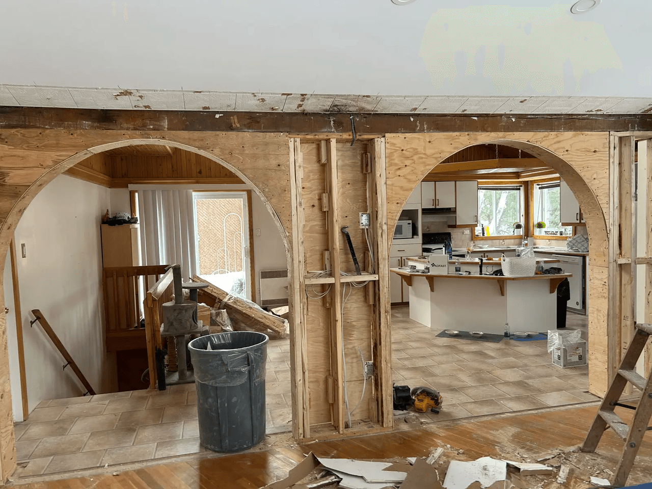 Rénovation intérieure avec murs ouverts, arches en bois, câblage apparent et cuisine en arrière-plan