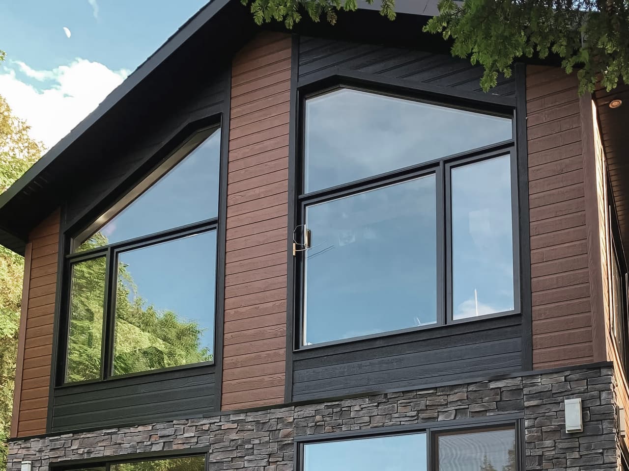 Façade moderne en bois et pierre dotée de grandes fenêtres allemandes de formes géométriques et triple vitrage.