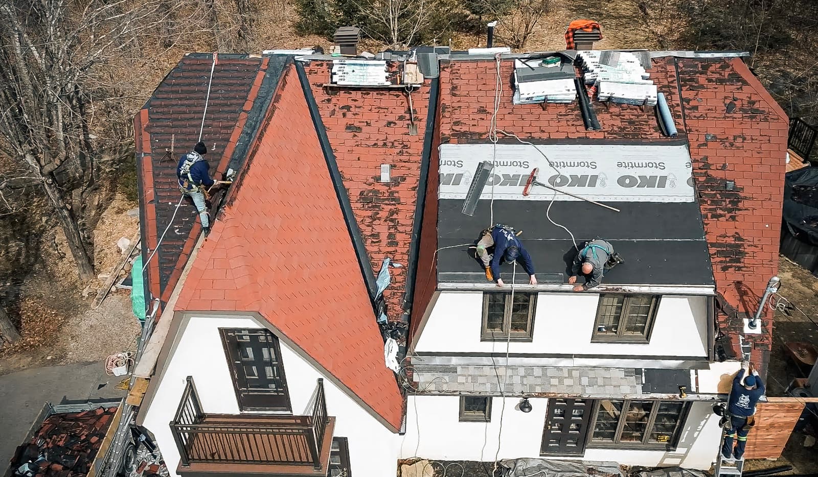 Travaux de rénovation de toiture avec installation de bardeaux rouges sur une maison à plusieurs étages.