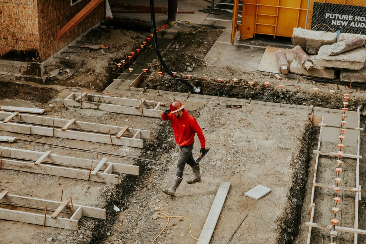 Travailleur de la construction marchant dans une excavation avec coffrage et armature pour fondation de bâtiment.
