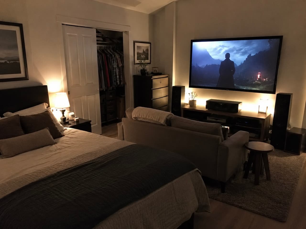 Chambre à coucher aménagée avec coin cinéma maison, grand téléviseur mural, système audio, canapé et éclairage d’ambiance chaleureux.