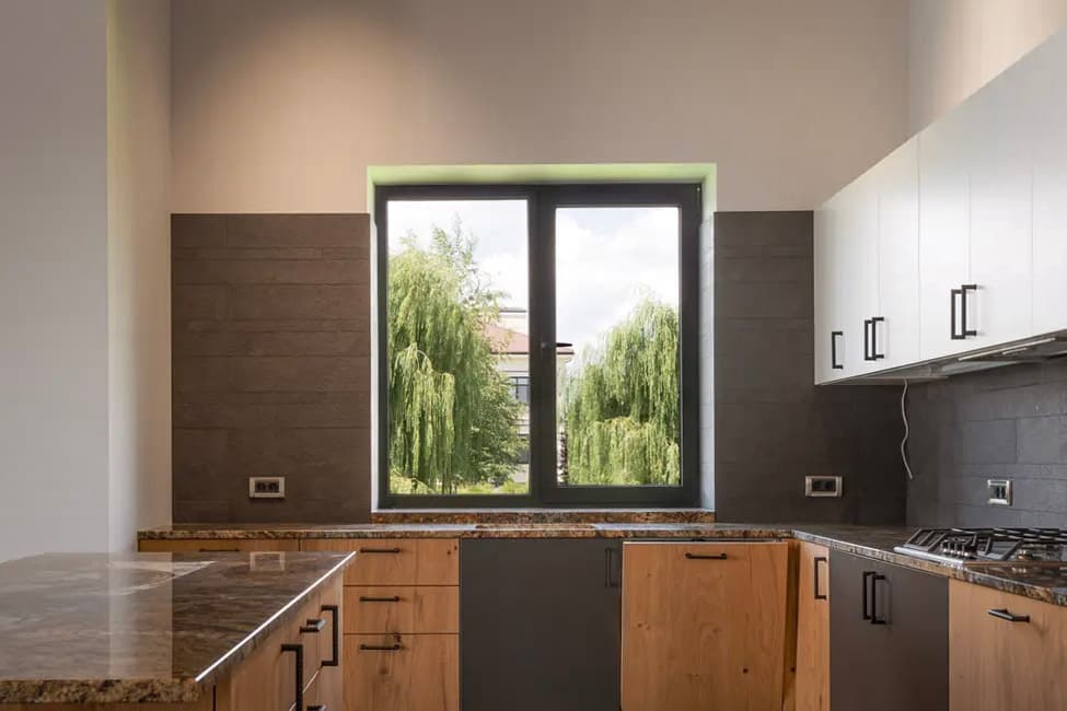 Cuisine moderne avec armoires en bois, comptoirs en granit, électroménagers intégrés et grande fenêtre offrant une vue panoramique.