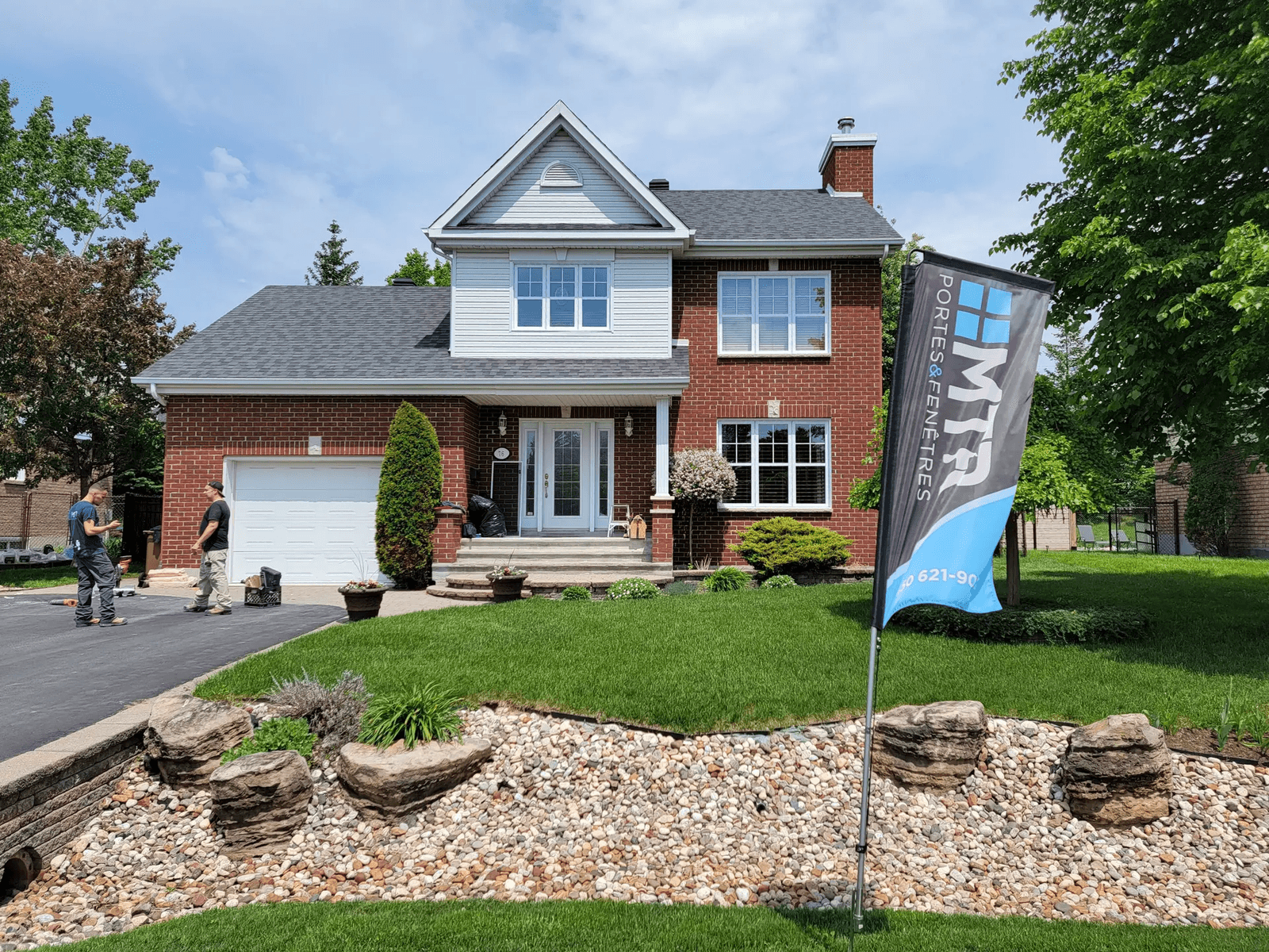 Maison familiale en brique rouge avec garage intégré, toiture en bardeaux, aménagement paysager soigné et parterre de pierres décoratives 