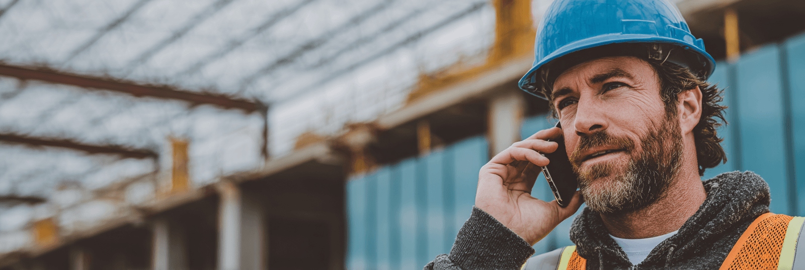 Entrepreneur en construction portant un casque bleu et un gilet haute visibilité, parlant au téléphone sur un chantier