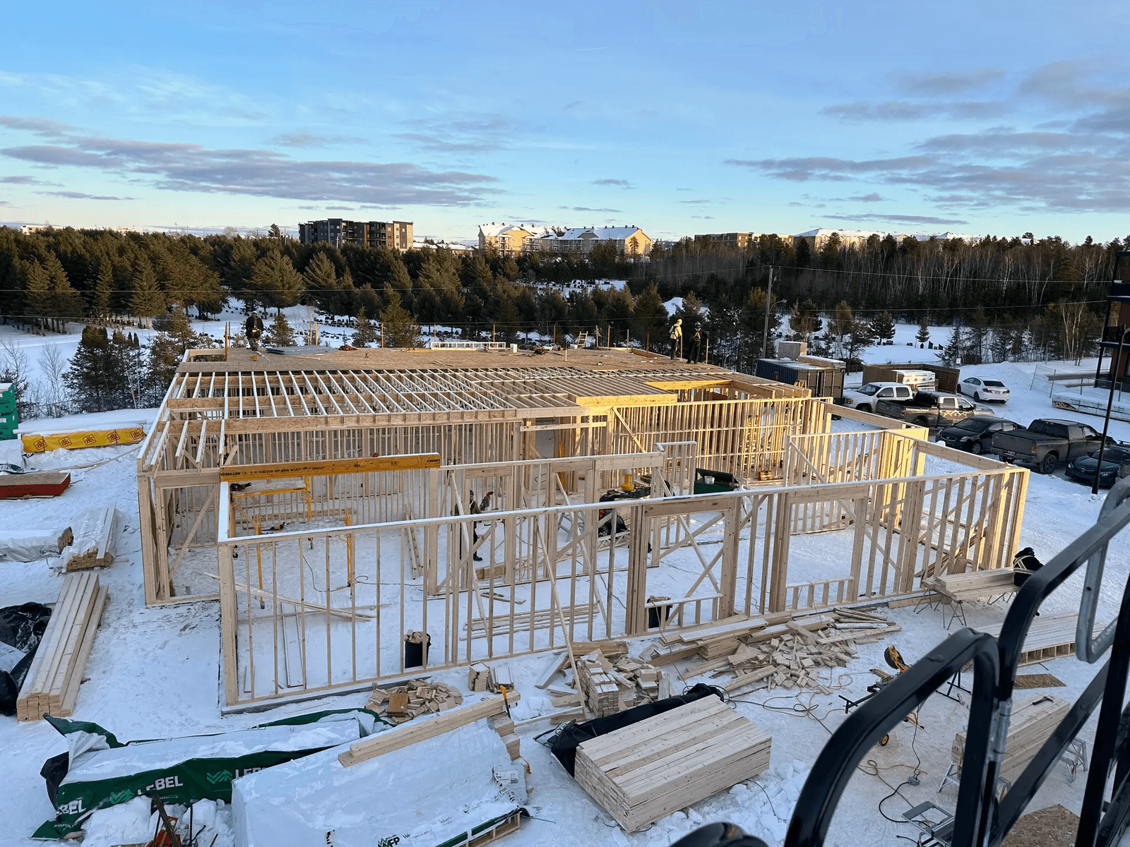 Vue d'un chantier de construction résidentielle avec une charpente en bois en cours de montage sur un site enneigé.