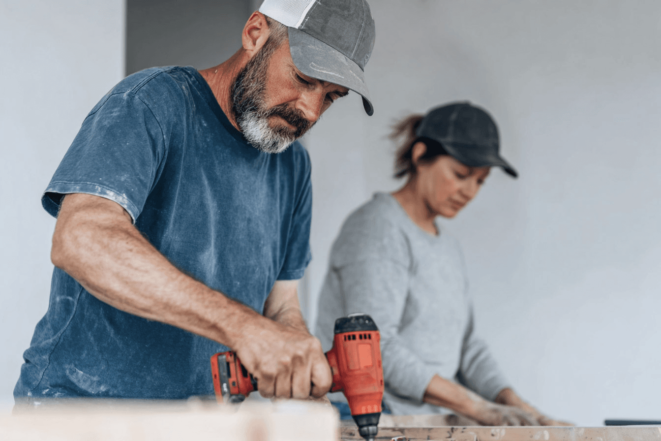 Travailleurs en rénovation intérieure utilisant une perceuse électrique et des outils sur une surface de travail dans une pièce en construction.