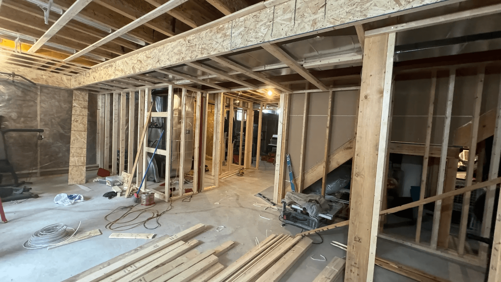 Sous-sol en rénovation avec ossature en bois, câblage électrique, et travaux de finition en cours. 