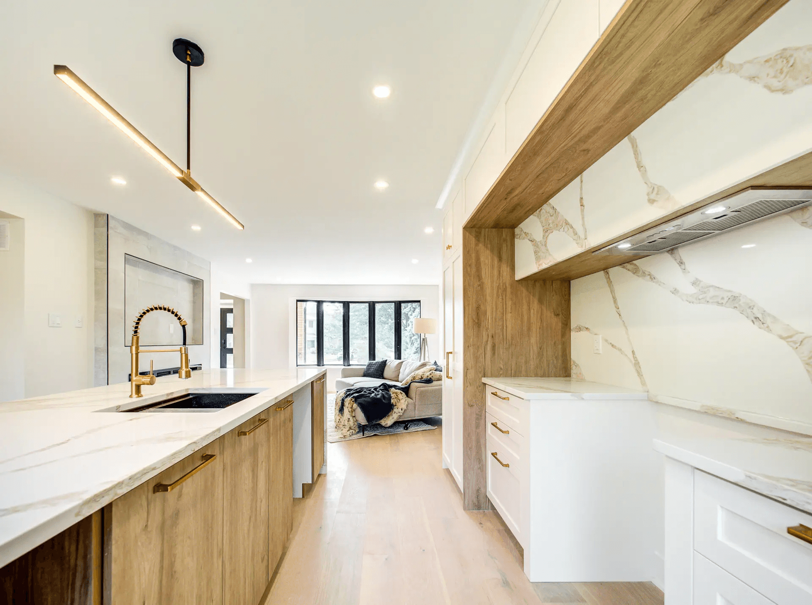 Cuisine moderne et lumineuse avec grand îlot en bois, comptoir blanc effet marbre, robinet doré, hotte intégrée et éclairage contemporain