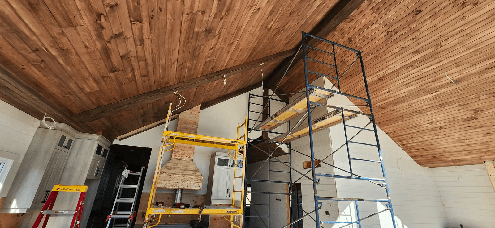 Rénovation intérieure en cours avec grand plafond cathédrale en bois, poutres apparentes, murs blancs, échafaudages et câblage électrique visible