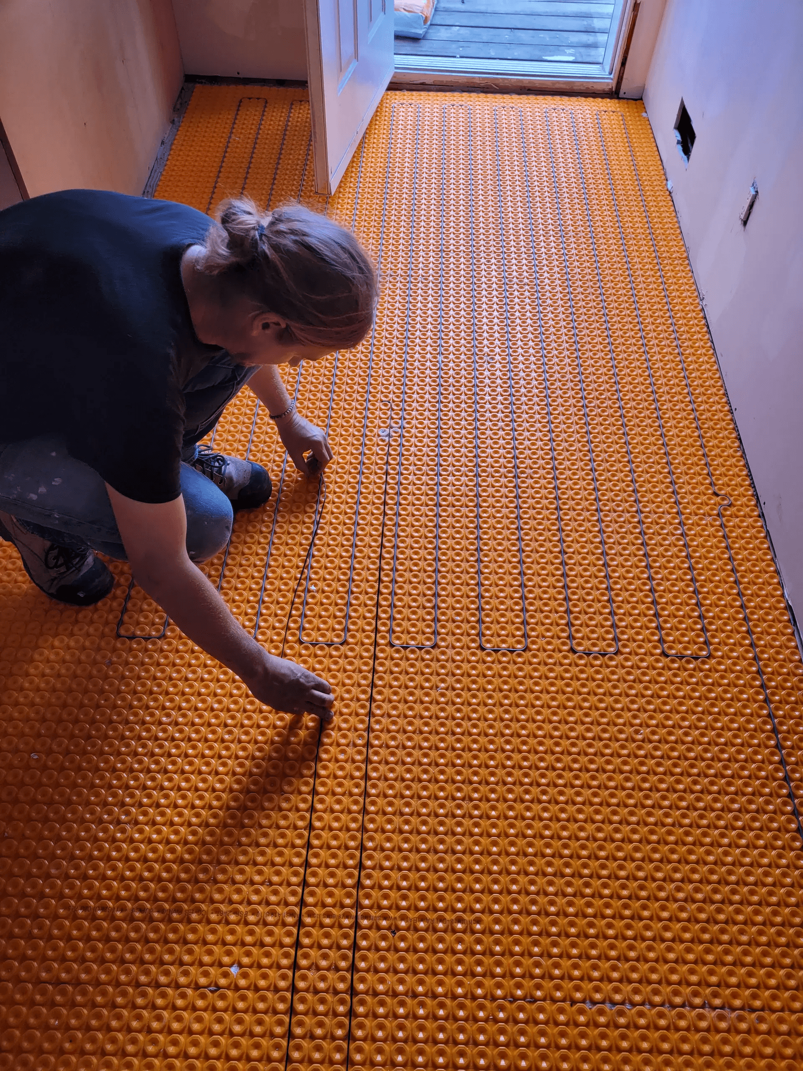 Travailleur installant un système de chauffage au sol électrique avec une membrane orange dans une pièce en construction.