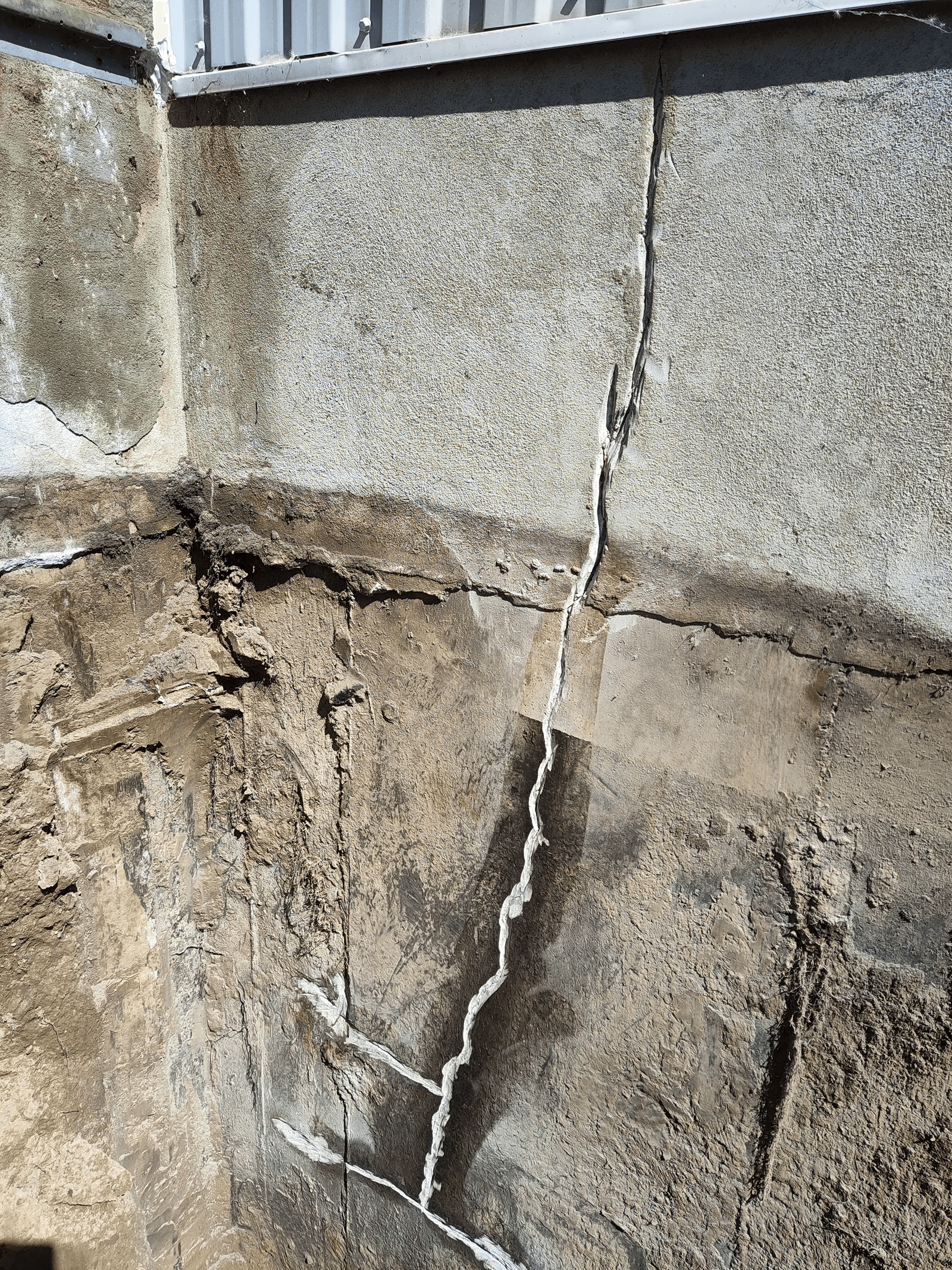 Fissure majeure en escalier sur une fondation en béton avec réparation par injection visible