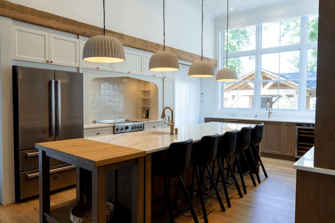 Cuisine moderne avec grand îlot central, armoires blanches et bois, réfrigérateur en acier inoxydable, luminaires suspendus et plancher de bois