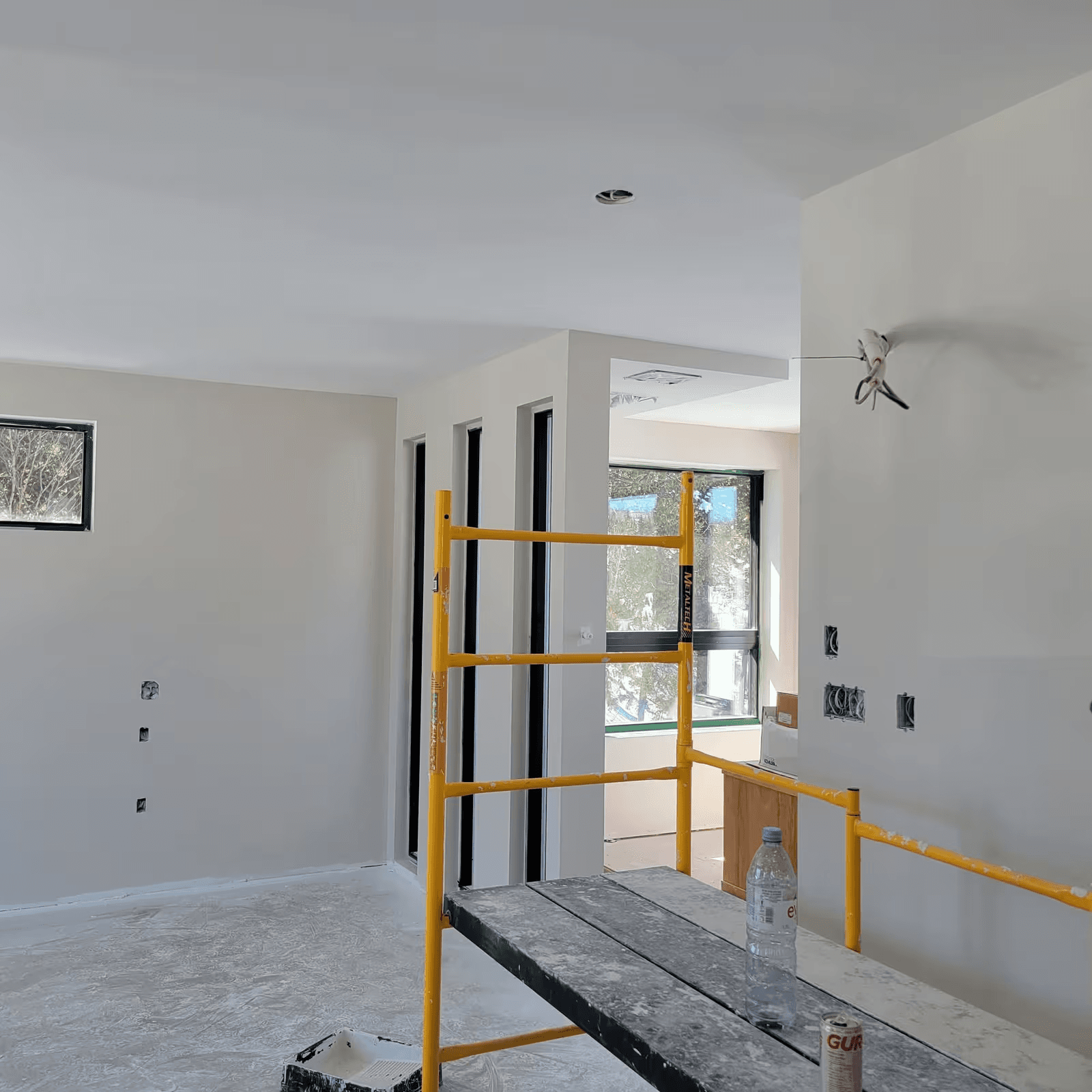 Pièce résidentielle en rénovation avec murs et plafond fraîchement finis, ouvertures électriques apparentes et échafaudage intérieur pour les travaux de finition