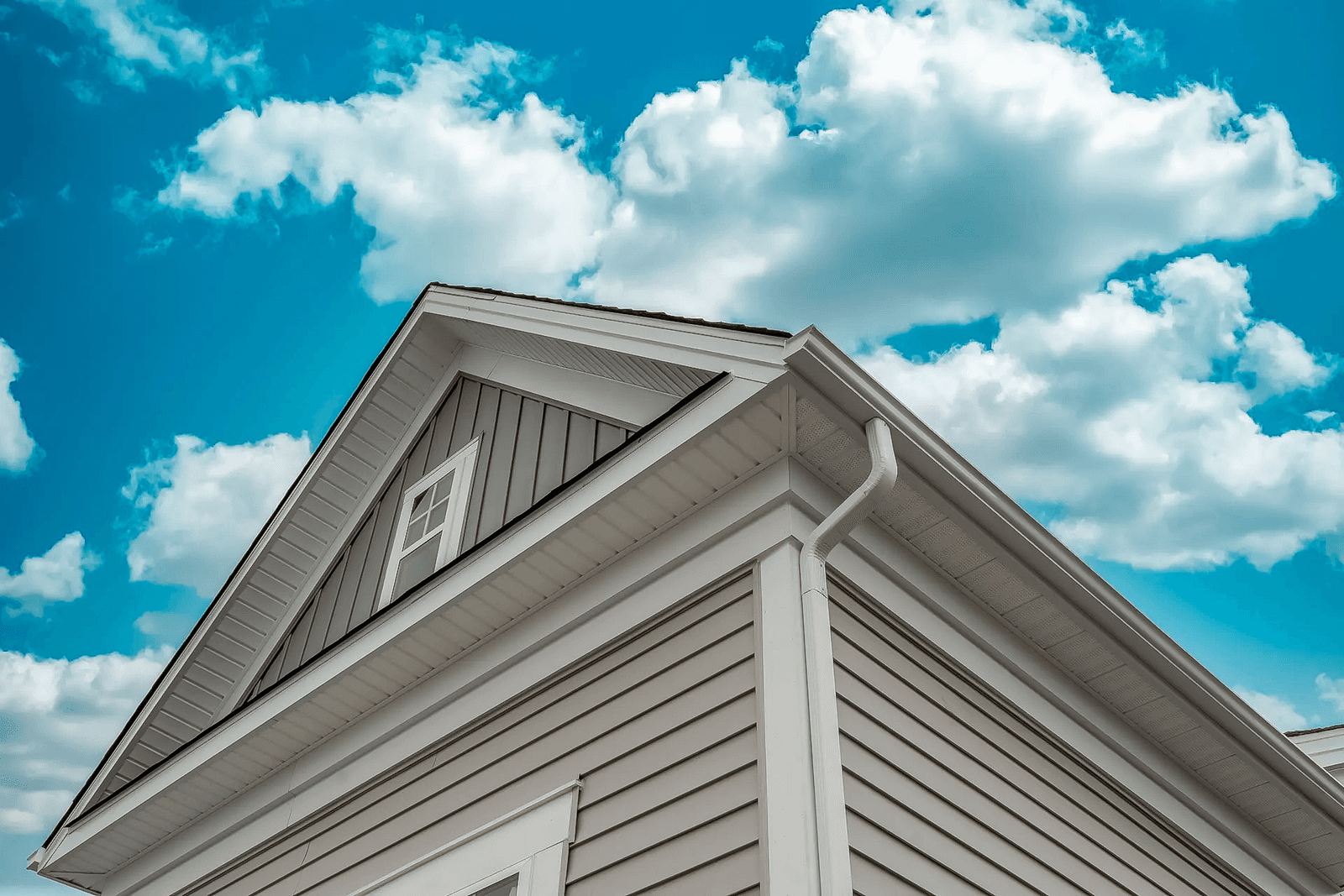 Maison au revêtement en vinyle beige, aux fenêtres blanches et aux gouttières, sous un ciel bleu nuageux.