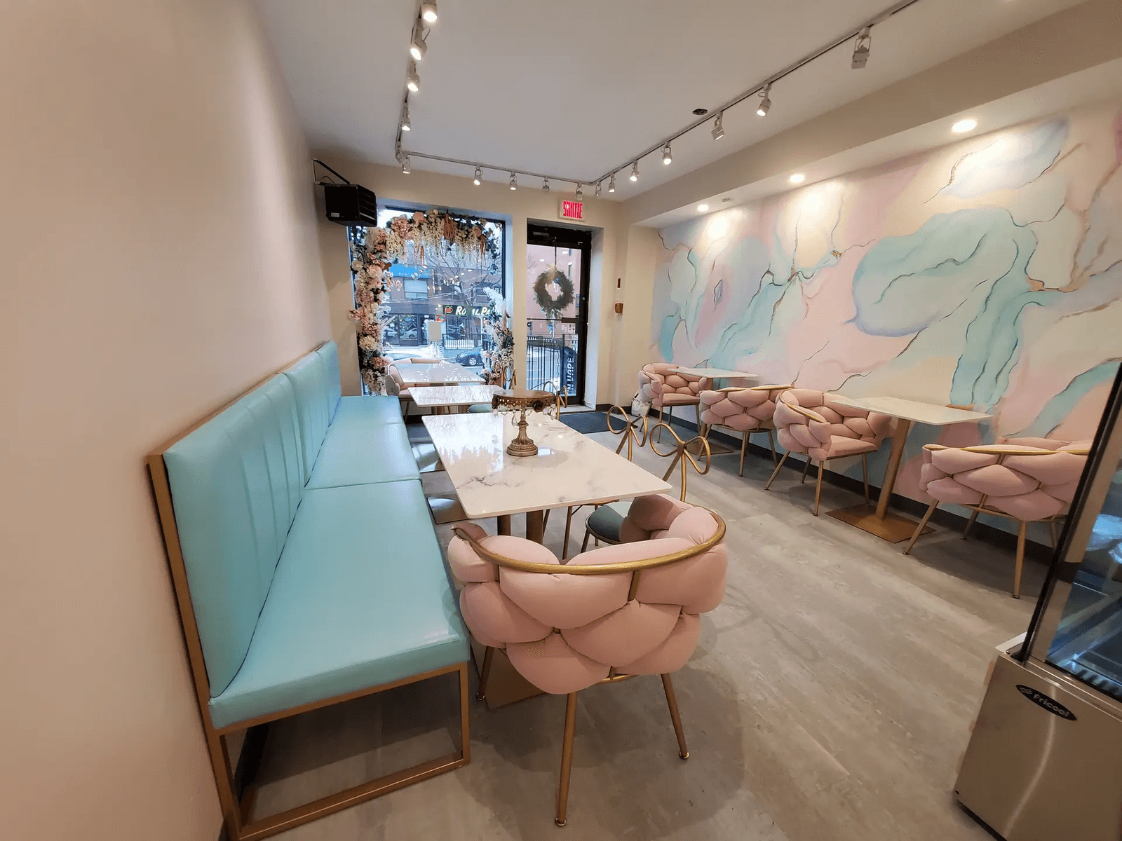  Intérieur de café ou restaurant moderne avec banquette turquoise, fauteuils roses, tables en marbre, éclairage sur rail et mur décoratif aux tons pastel