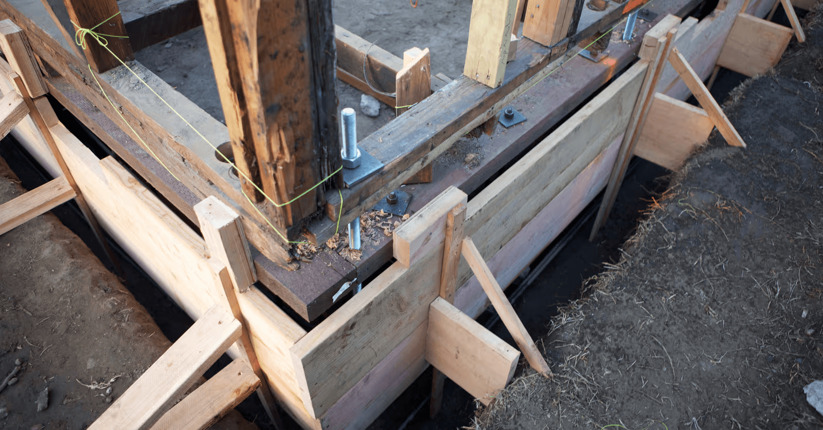 Coffrage en bois et renforcement structural autour de poteaux de maison lors de travaux de fondation et de rénovation.