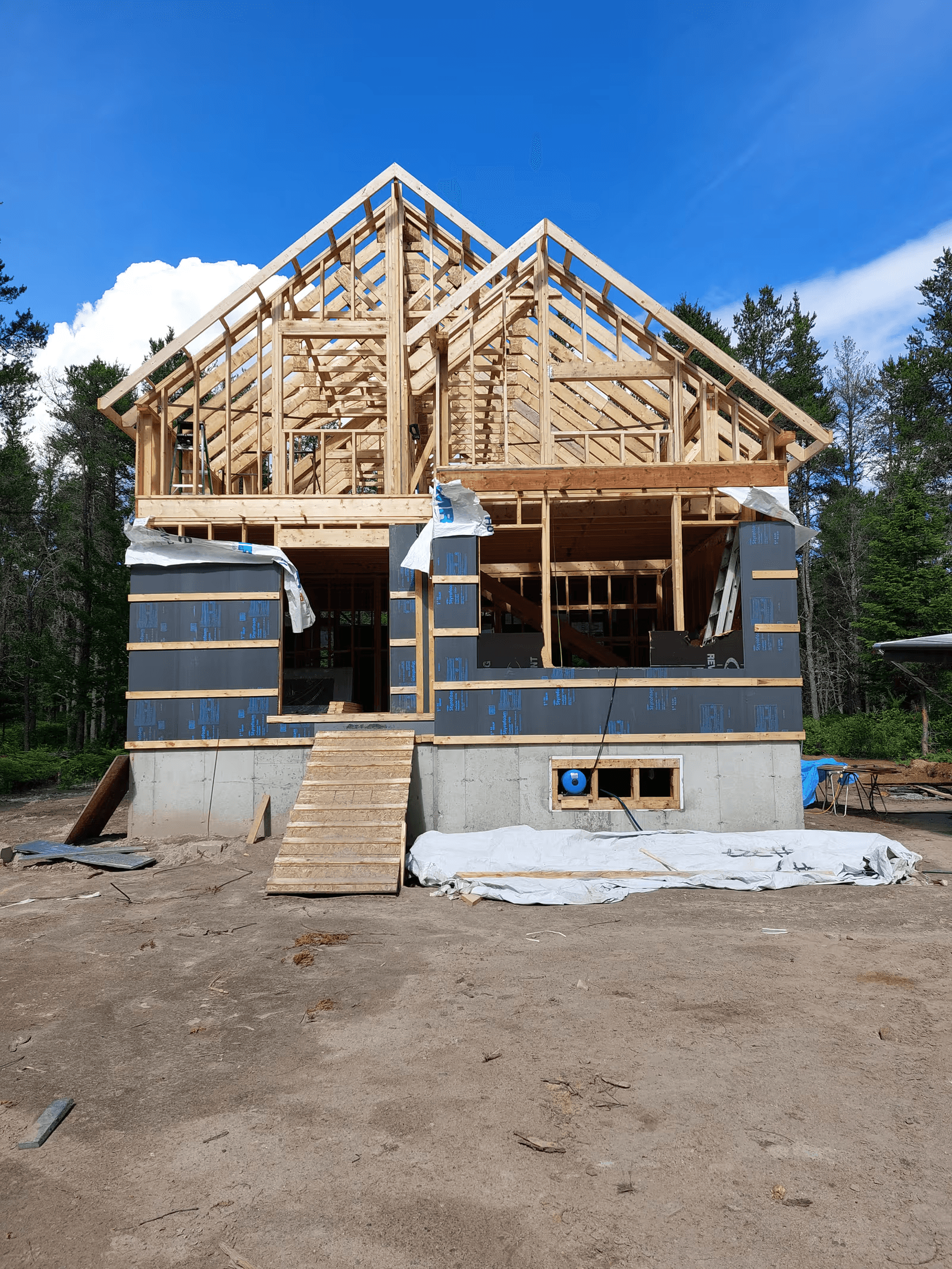 Maison neuve en construction avec charpente complète en bois, fermes de toit apparentes, fondation en béton et enveloppe extérieure partiellement installée