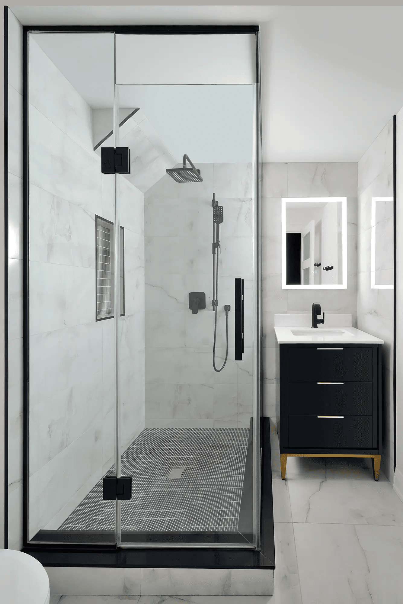 Salle de bain moderne rénovée avec douche vitrée, céramique effet marbre blanc, robinetterie noire et vanité noire avec miroir lumineux