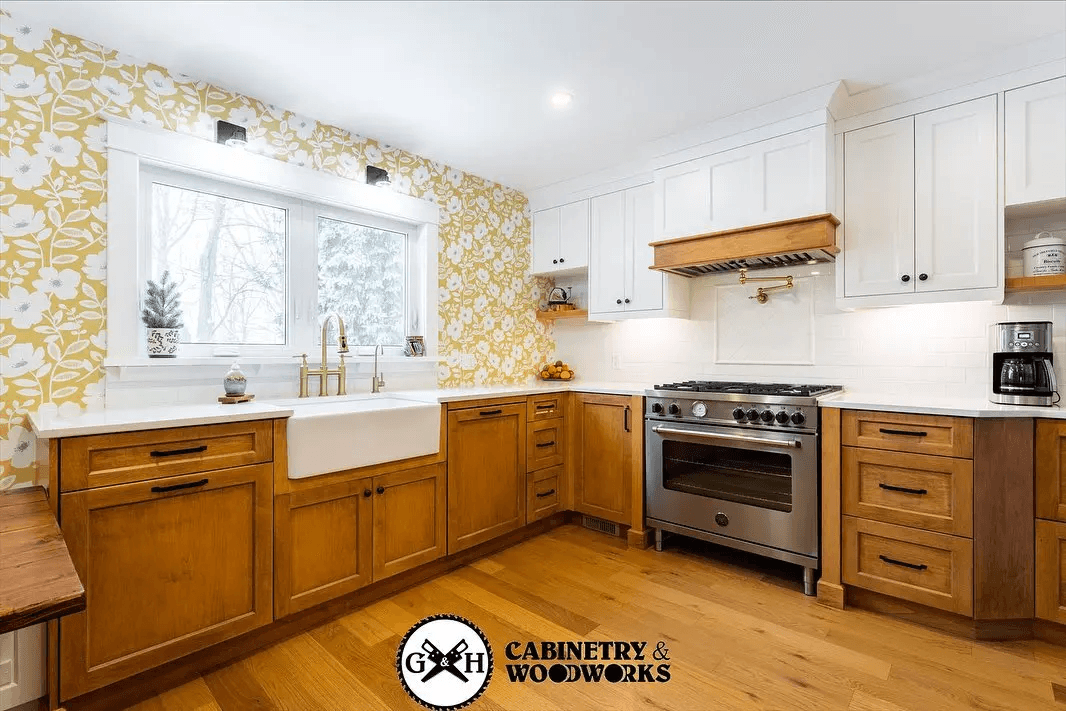 Cuisine rustique avec armoires en bois, papier peint floral jaune, évier farmhouse blanc, comptoirs en quartz blanc, et cuisinière en acier inoxydable.