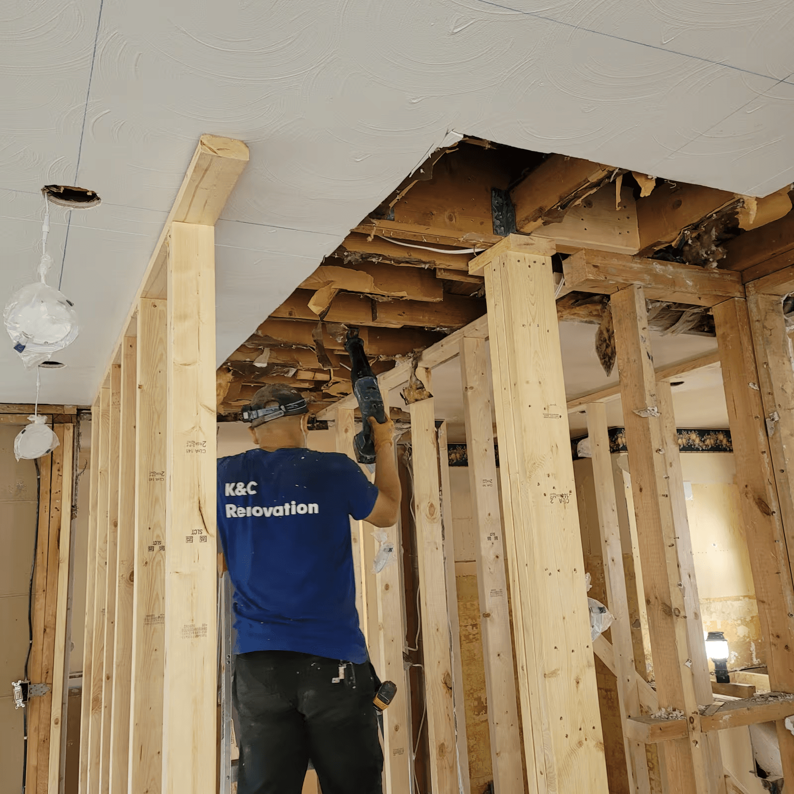 Travailleur en rénovation intérieure utilisant un outil électrique sous un plafond ouvert, avec nouvelle ossature de bois et structure apparente