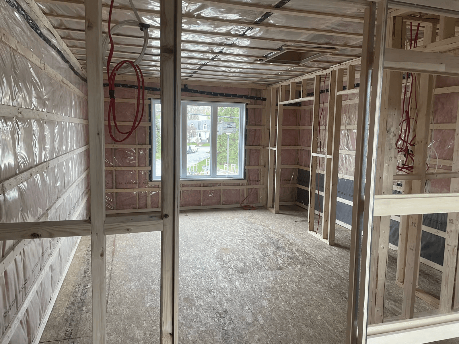 Pièce résidentielle en construction avec ossature de bois apparente, isolation en fibre de verre, pare-vapeur, câblage électrique et fenêtre installée.