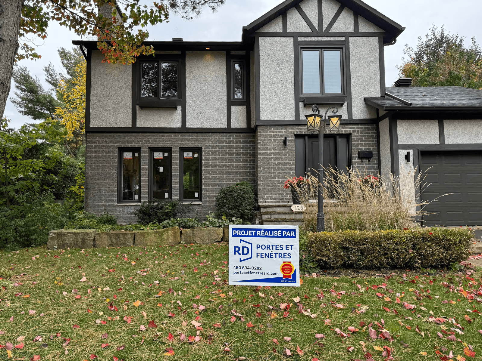 Façade rénovée d’une maison résidentielle avec nouvelles fenêtres foncées, porte d’entrée, garage, revêtement extérieur contrasté et aménagement paysager automnal.