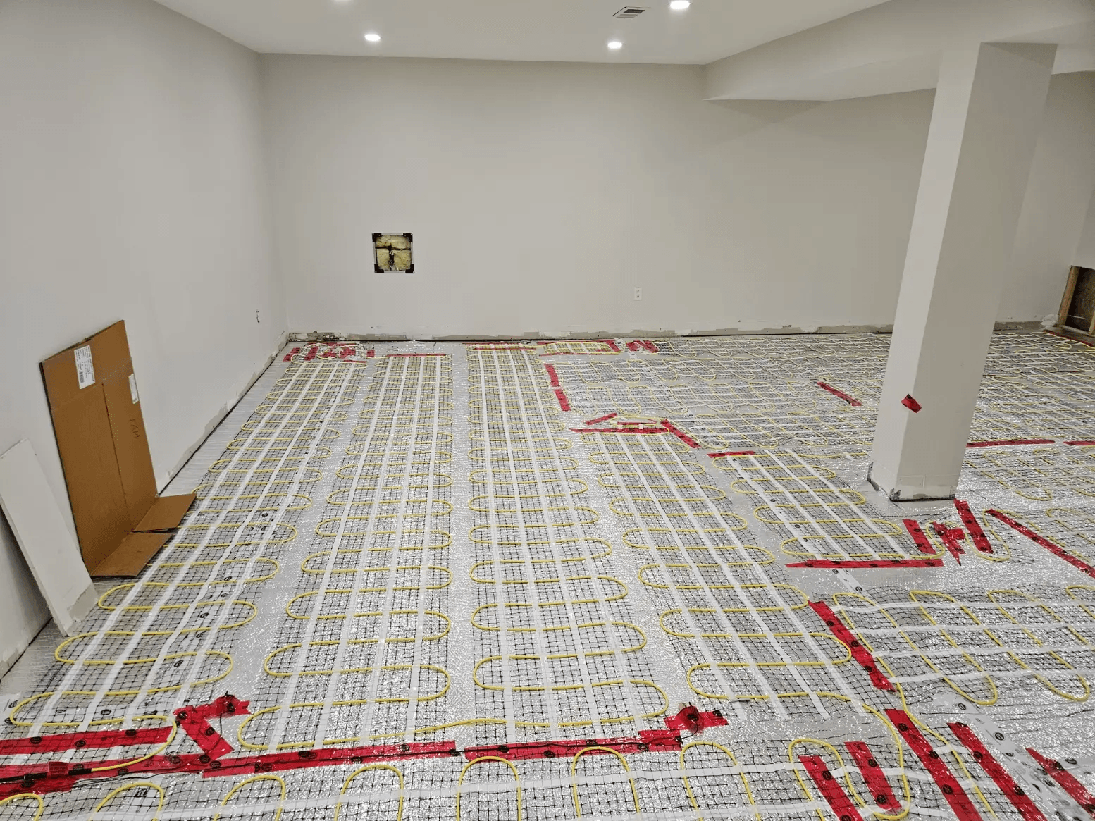 Installation de plancher chauffant électrique avec câbles chauffants jaunes fixés sur une membrane isolante dans un sous-sol en rénovation