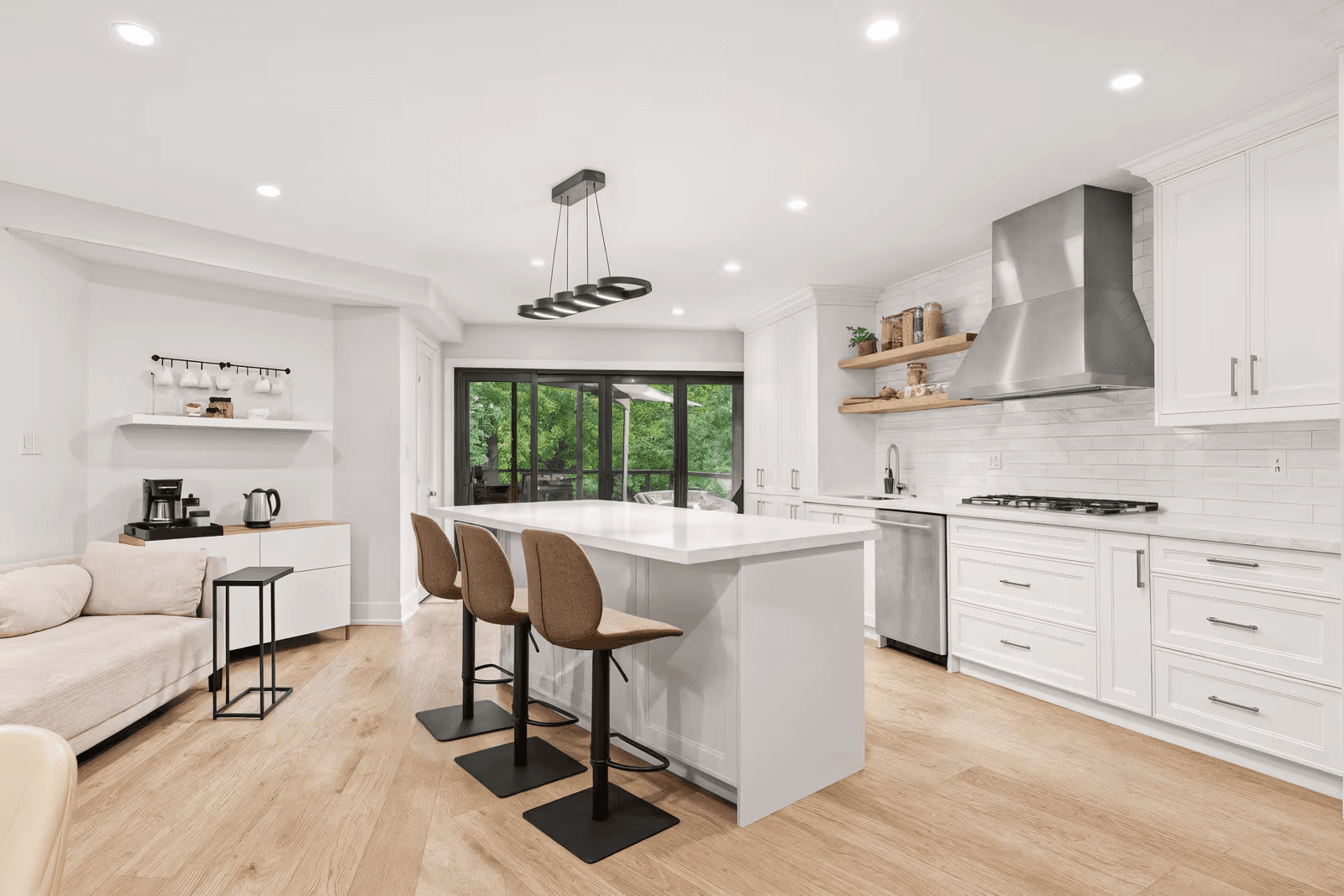 Cuisine moderne blanche avec grand îlot central, tabourets, hotte en acier inoxydable, armoires sur mesure et plancher de bois clair