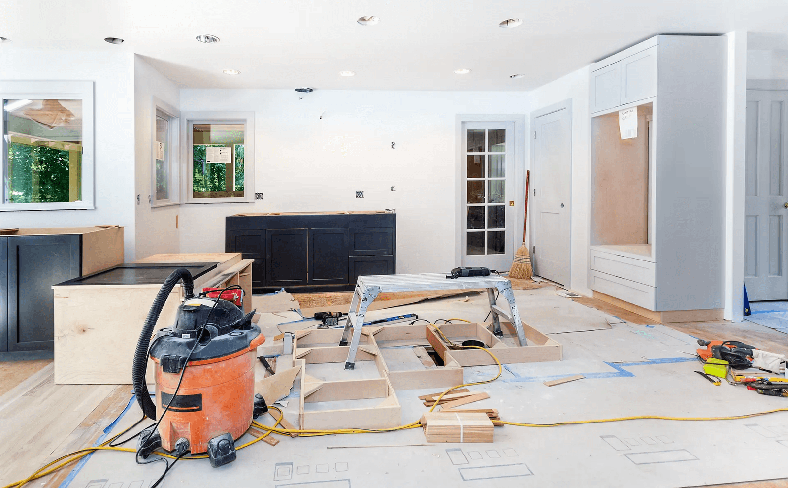 Cuisine en pleine rénovation avec installation d'armoires, outils de construction et plancher en cours d'aménagement.