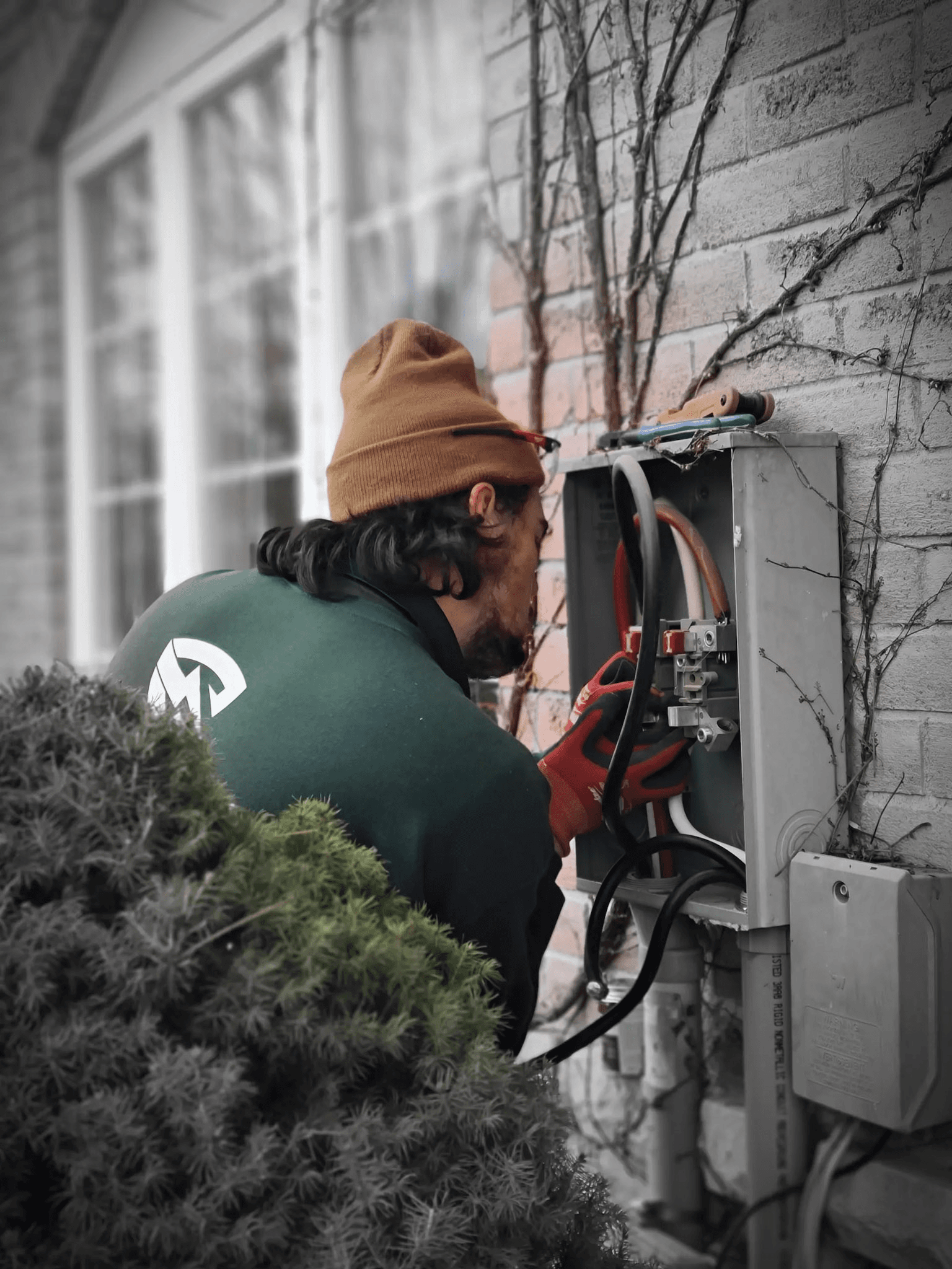 Un électricien effectuant des réparations sur une boîte électrique extérieure attachée à un mur en brique.