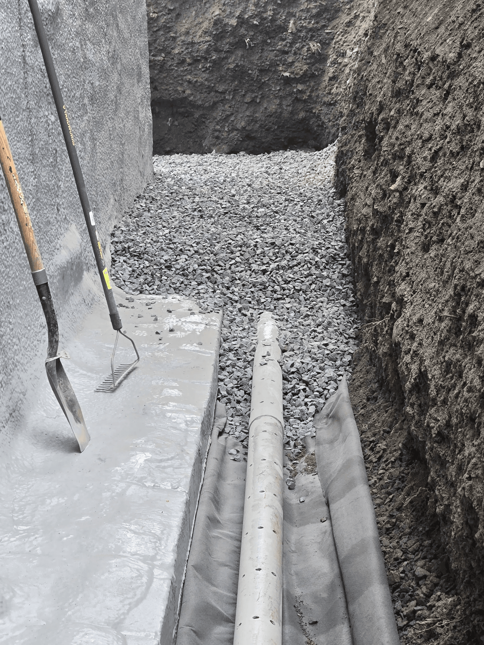 Vue rapprochée d’un drain français en cours d’installation avec membrane géotextile et gravier le long d’une fondation