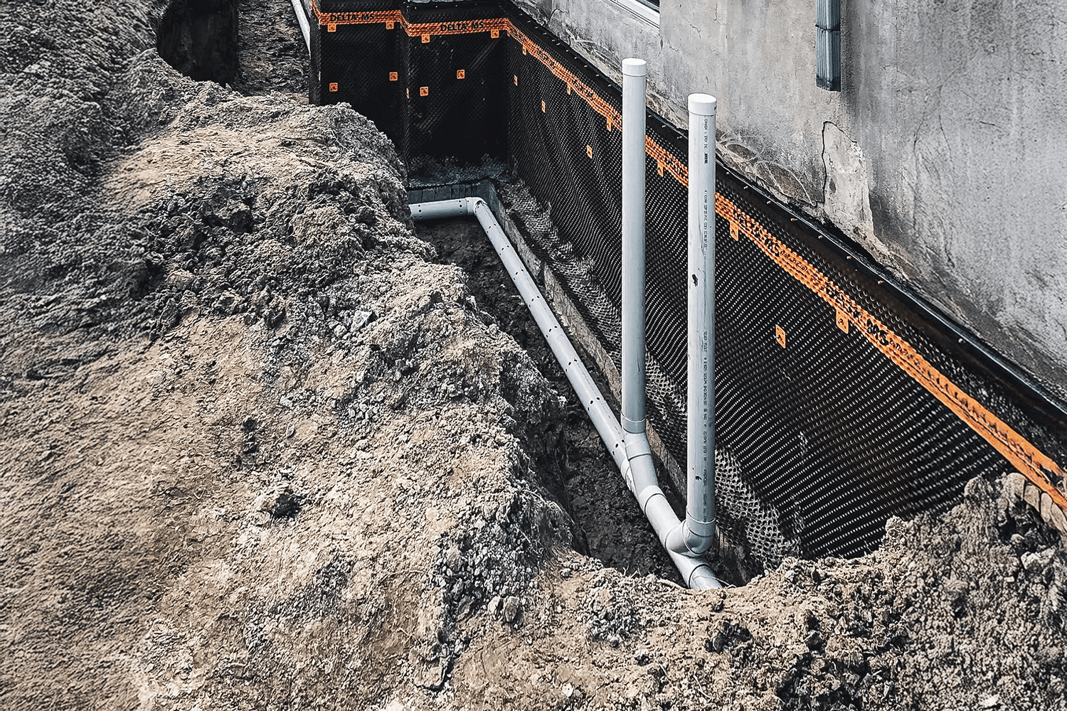 Travaux d'excavation pour l'installation d'un drain français et d'une membrane d'étanchéité sur la fondation d'une maison.
