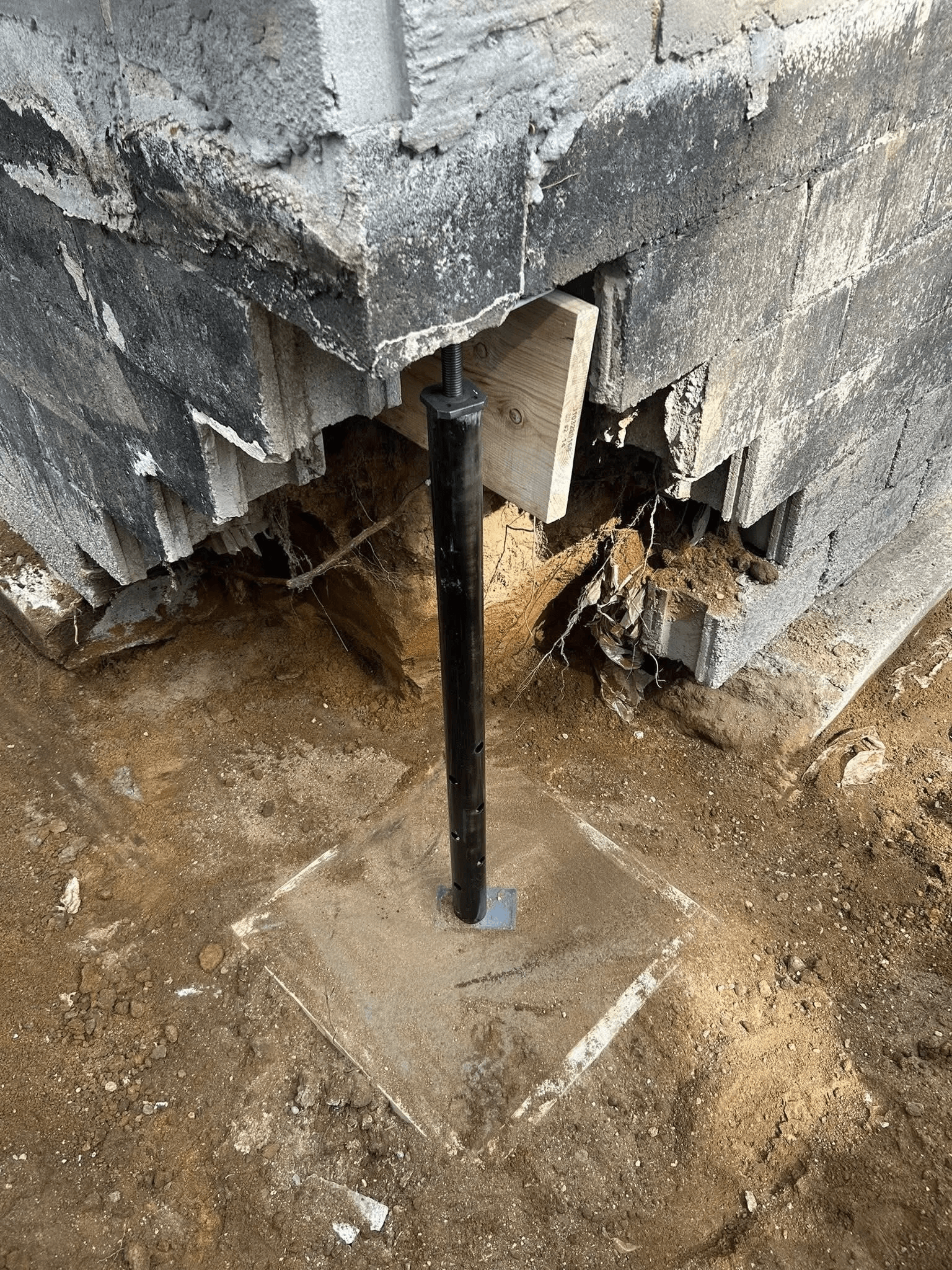 Réparation d’une fondation en blocs de béton endommagée avec poteau de soutien métallique réglable installé sur une semelle de béton.