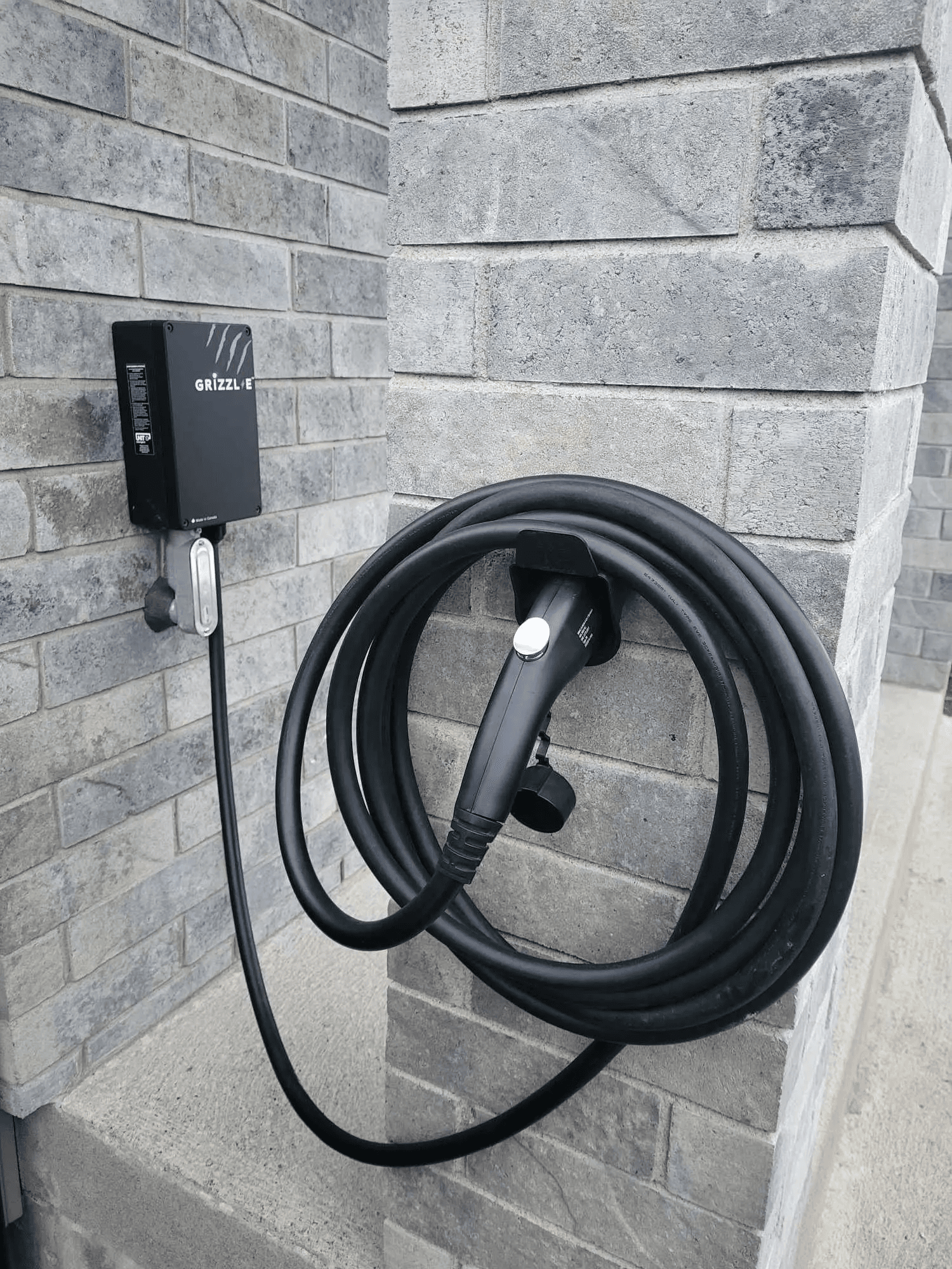 Borne de recharge résidentielle pour véhicule électrique installée sur un mur de brique, avec câble de recharge enroulé et connecteur mural
