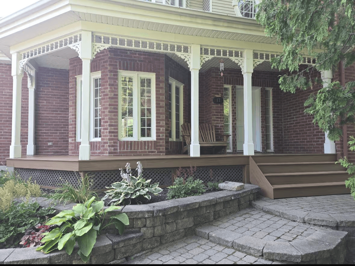 Façade de maison en brique avec grand porche couvert, colonnes blanches, escalier extérieur, pavé-uni, muret et aménagement paysager