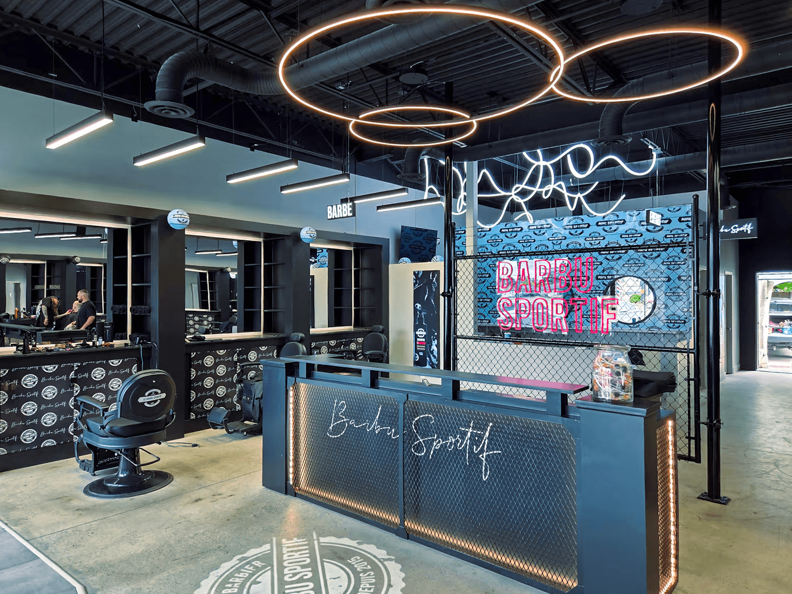 Modern barbershop interior with barber stations, chairs, reception counter, circular pendant lighting and industrial decor