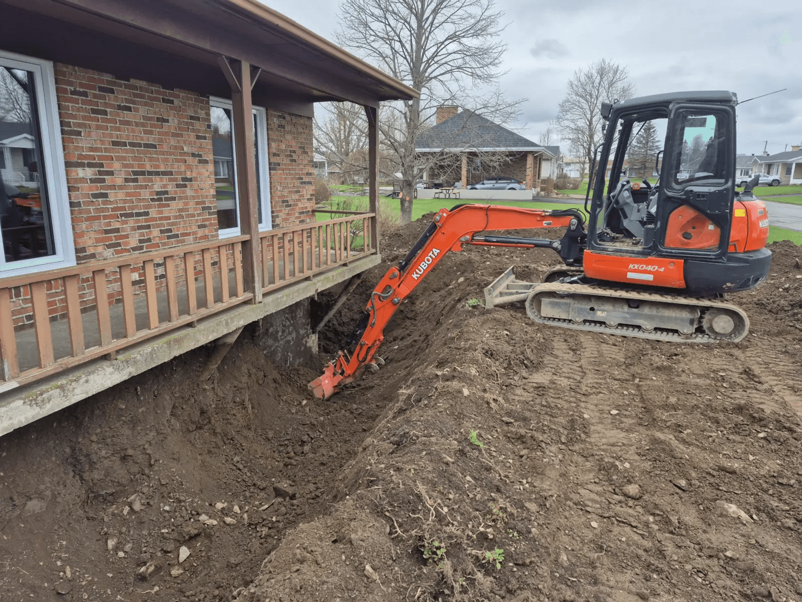 Travaux d’excavation avec mini-pelle pour dégagement de la fondation d’une maison en brique en vue d’une imperméabilisation ou d’un remplacement de drain français.